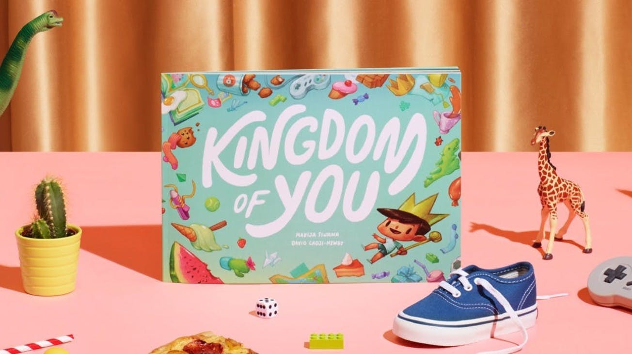 The Kingdom of you book sitting on a desk with different items surrounding it, such as cactus, lego, dice and pizza